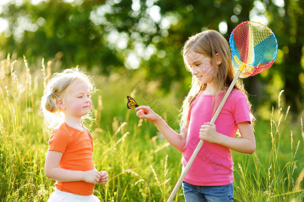 两个小姐妹用勺子网捉蝴蝶和虫子。在阳光明媚的夏日探索大自然的孩子们.