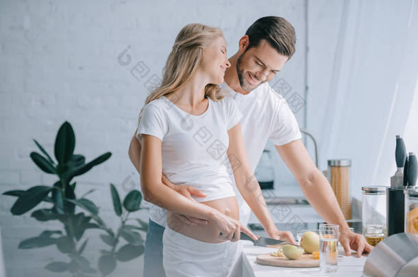 愉快的孕妇和丈夫烹调果子沙拉一起在厨房在家
