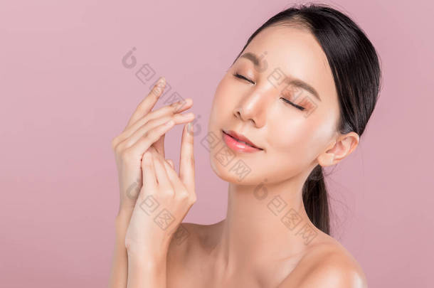 年轻快乐美丽的亚洲女人闭上眼睛，<strong>微笑</strong>着牵着她的手，手部皮肤护理理念，与粉红的背景隔离.