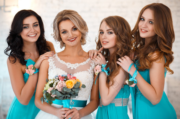 新娘和三个伴娘在相似的蓝色连衣裙，有完美的化妆和发型在光的阁楼空间