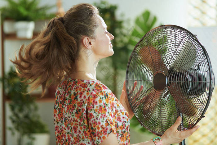 夏天的炎热。在阳光灿烂的夏日里，穿着花衣的40岁的现代女人在现代客厅里欢呼雀跃.