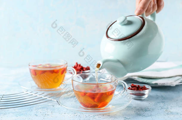 女人从茶壶里倒入桌上的杯子里，倒入美味的茶。
