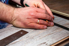 在家里安装新的木质复合地板时使用测量弯头和铅笔的人.