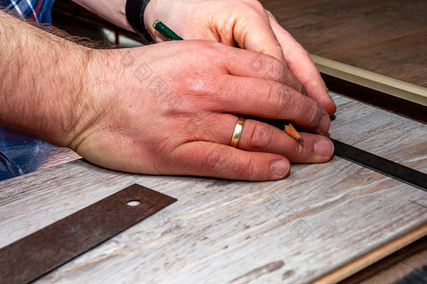 在家里安装新的<strong>木质</strong>复合<strong>地板</strong>时使用测量弯头和铅笔的人.