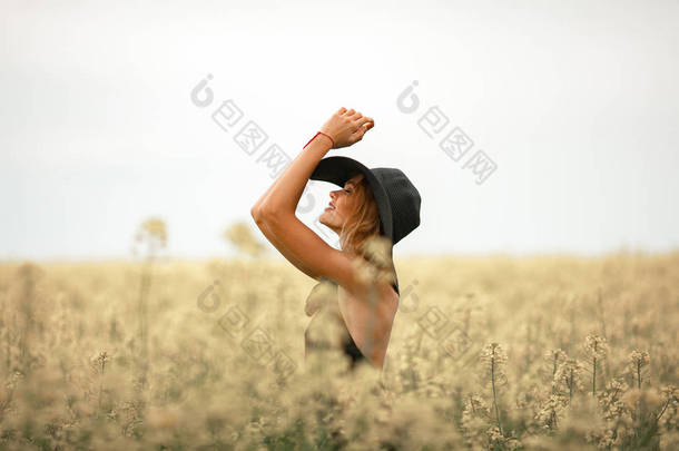 黑色的衣服和帽子之间开花草甸的年轻女子.