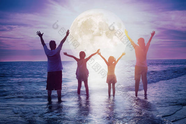 家人站在沙滩上看月亮。庆祝中年