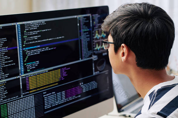 坐在办公桌前时，戴着眼镜的聪明的少年在电脑屏幕上检查编程代码