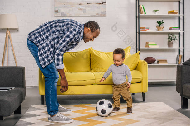 快乐的年轻父亲看着微笑的小儿子在家里玩足球