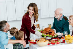 快乐的成年妇女和高级男子携带烤火鸡感恩节庆祝与家庭在家里 