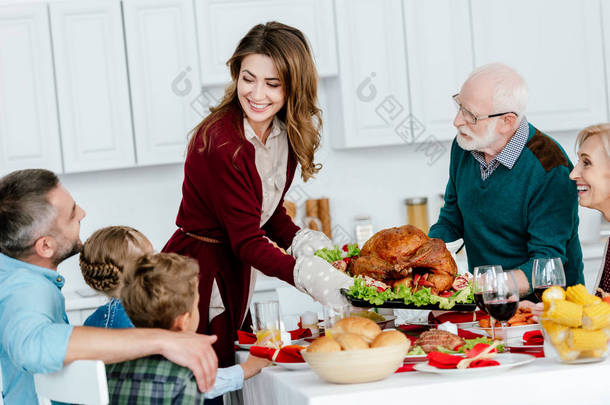 快乐的成年妇女和高级男子携带烤火鸡感恩<strong>节庆</strong>祝与家庭在家里 