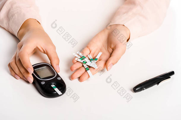 妇女持有血糖仪和条查出的白色, 糖尿病概念的裁剪图像