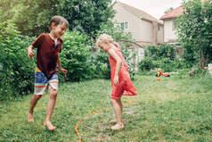 孩子朋友男孩女孩泼水与园艺软管洒水器在后院在夏天的一天。孩子们在家院子外面玩水。坦率真实的现实生活时刻有趣的家庭活动