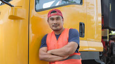 一个亚洲人在黄色的卡车旁边快乐地微笑着。他有一个运输司机的职业.运输业从未停止过。它必须是驱动和旅行所有的时间.
