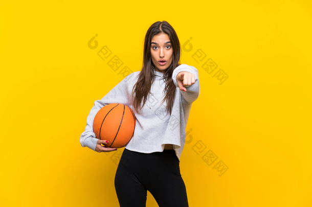 年轻<strong>女子</strong>打篮球在孤立的黄色背景惊讶和指向前面