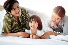 快乐的家庭在卧室里玩的开心。父亲、母亲和女儿躺在床上，在一起度过时光，父母和孩子都有很好的记忆力，在家里玩耍 