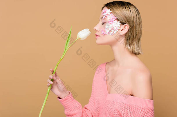 有吸引力的女人的侧视图与鲜花在脸上闻到郁金香孤立在米色