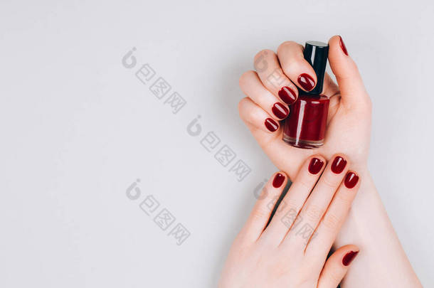 漂亮的深红色美发与一瓶指甲油在灰色背景的手。<strong>程序</strong>概念。平铺风格.