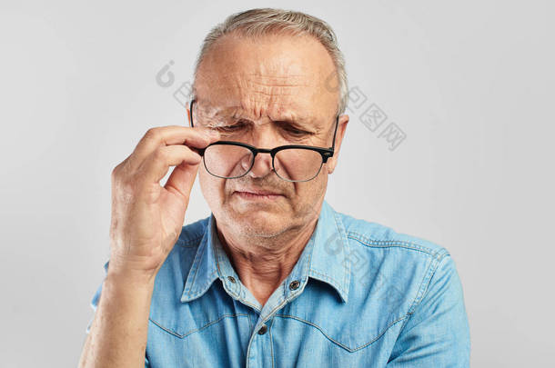 视力问题。一位老人摘下眼镜。不满意。穿着蓝色衬衫的白色背景的老人。光学