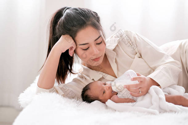 美丽的亚洲母亲躺在白色的床上，给她的新生儿喂牛奶.