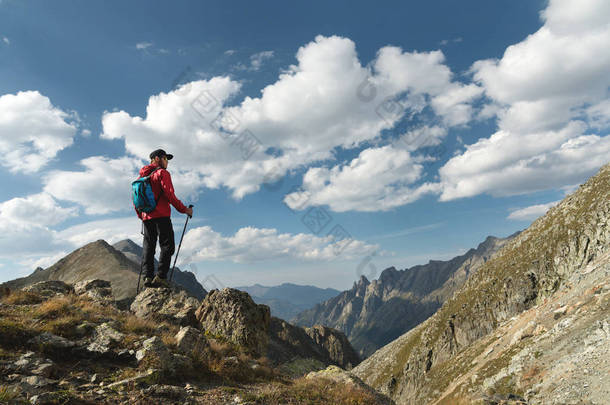 一个戴着太阳镜的胡子男人和一顶带背包的帽子矗立在一块岩石上, 看着山中的一个岩石山谷。旅游理念与山区户外休闲徒步