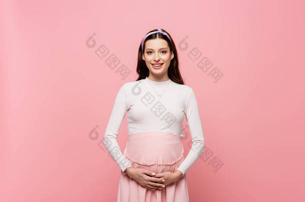快乐的年轻漂亮孕妇摸着被粉色隔离的肚子