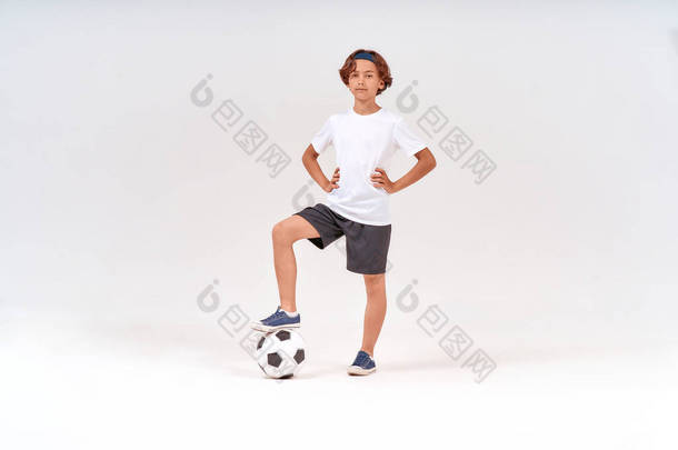 足球运动员。一个快乐的少年，戴着足球，看着镜头，笑着站在灰蒙蒙的背景下，全景全景拍摄