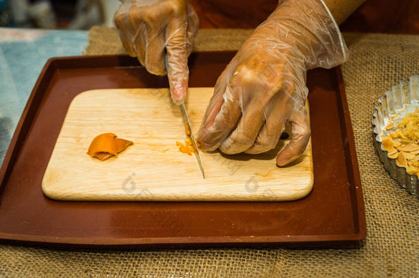 用刀割干的橘皮在木制切割板上对一个女人的手的特写。粮食概念