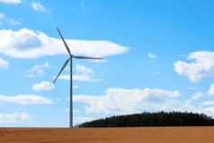 一杆和风车的风力发电站，在蓝天白云下，靠近森林和玉米地的乡村.