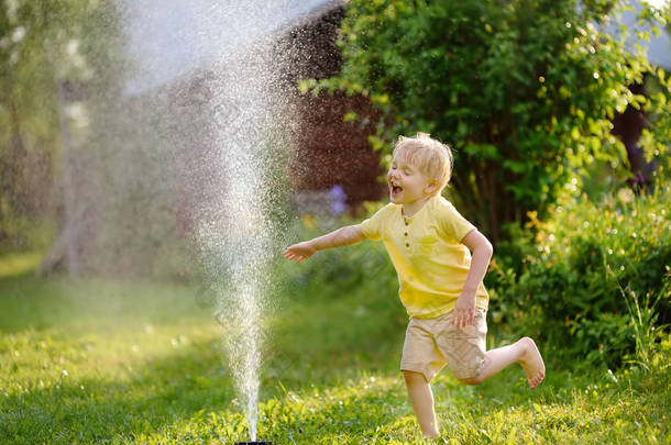 在阳光明媚的后院玩花园洒水车的滑稽小男孩。学前儿童玩喷雾水的乐趣。儿童夏季<strong>户外</strong>活动.