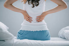 从床上背部疼痛的穿着睡衣的年轻女子的背部视图