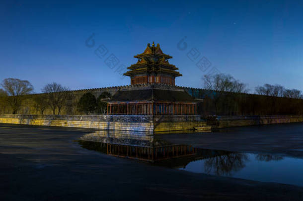 位于中国北京的紫禁城故宫博物馆的西北塔和城墙的全景夜景，反映在半冰冻的护城河上