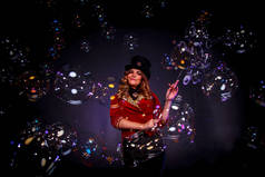 穿着舞台服头戴礼帽的女孩.女魔术师，一个穿着戏剧化服装的魔术师，用黑色背景的肥皂泡作秀。戏剧表演的概念