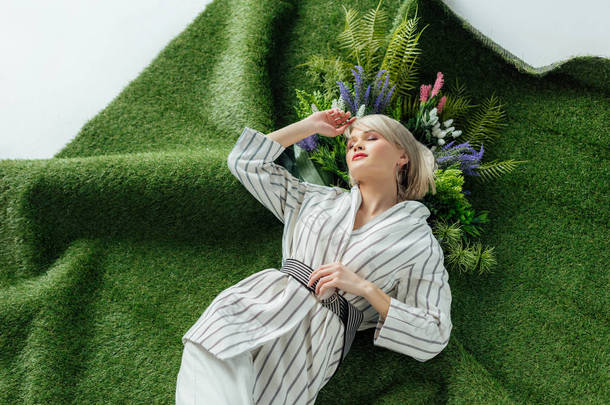 美丽的时尚女孩躺在人造草地上与蕨类植物和鲜花