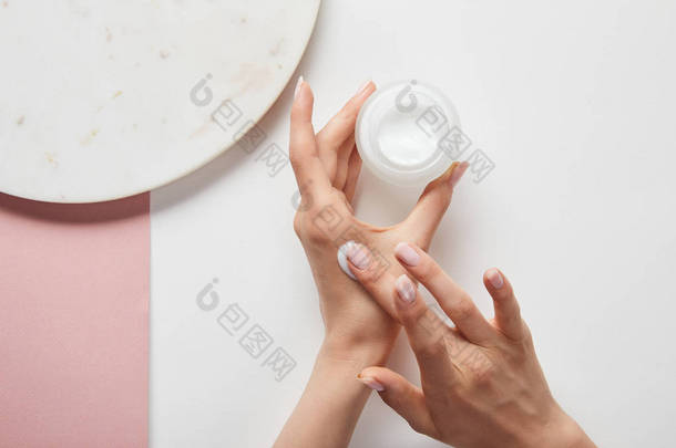 裁剪视图的妇女拿着奶油在罐子里，在皮肤上涂上化妆品