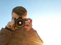 一个带着照相机的年轻人的肖像。那个人正在看摄影机。用太阳光线对着蓝天的肖像。概念.