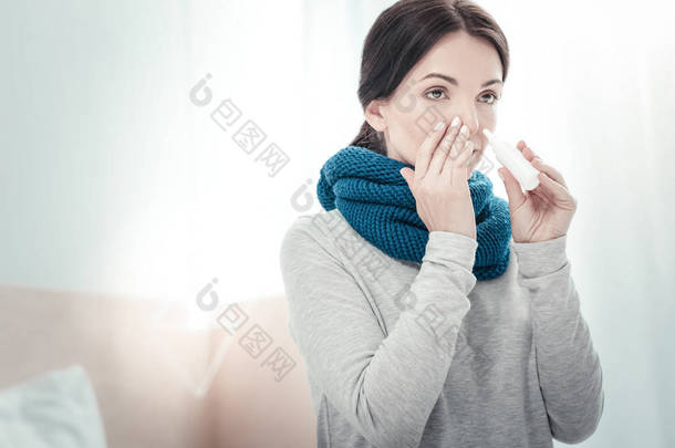 严重患病妇女使用鼻喷雾触摸她的鼻子.