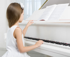 小女孩在弹钢琴的白色连衣裙的侧视图