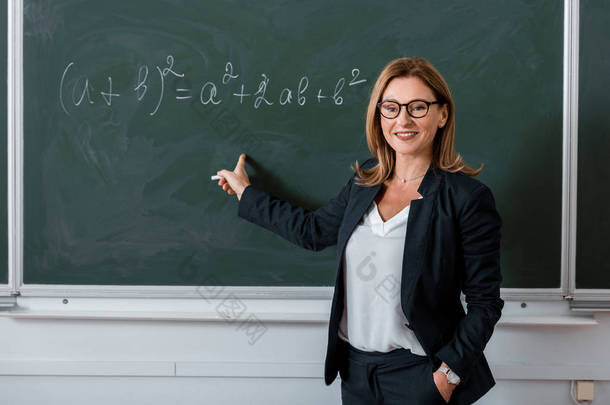 女教师用手指指着黑板上的数学方程在课堂上
