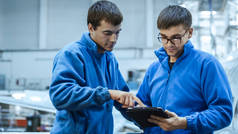 两架飞机维修技工有交谈时在飞机库中使用一台平板电脑.