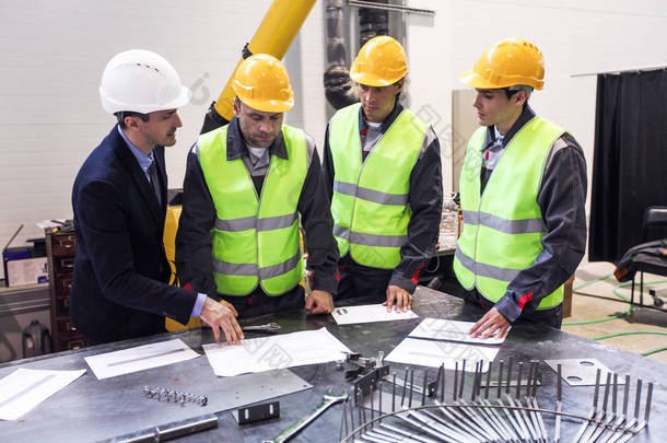 工程师、 领班和配戴<strong>安全</strong>帽的工人正在开厂和讨论文件，并在表 bluprints