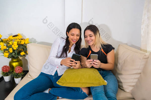 两个朋友坐在客厅的沙发上玩智能手机的网络游戏
