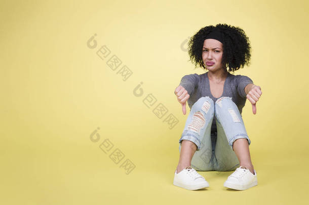失败的概念与女人：不成功的沮丧的女人用拇指向下与悲伤的外观孤立的黄色背景与空白的复制空间.