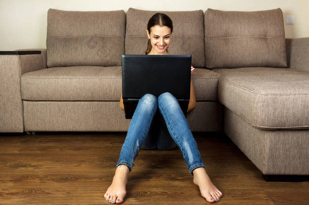 漂亮的女孩坐在用她的笔记本电脑在家里，在客厅里的地板上
