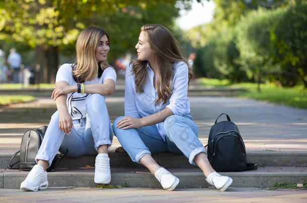 两个漂亮的年轻女孩坐在台阶上。女朋友们夏天在城市里休息.