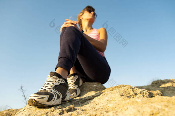 女徒步旅行者坐在陡峭的大石头上，享受温暖的夏日。年轻的女登山者在大自然的体育活动中休息。自然中的积极娱乐概念.