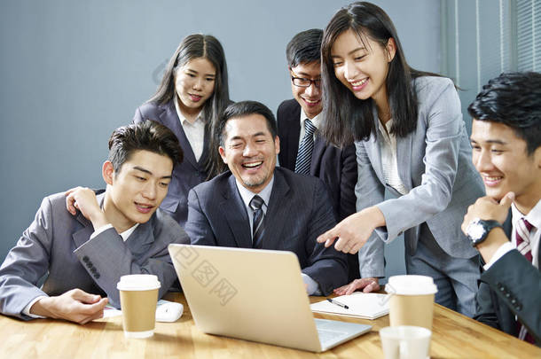 一支由亚洲企业高管组成的团队, 使用膝上型电脑在<strong>办公室工作</strong>, 快乐和微笑.