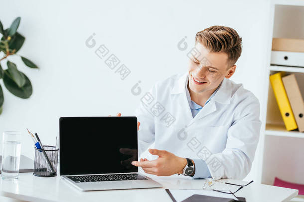 快乐的医生用手指指着笔记本电脑，屏幕空白 