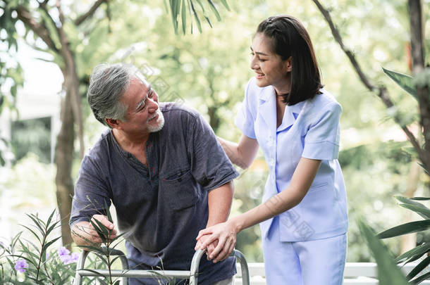 护士与病人使用沃克在退休回家。<strong>年轻</strong>的<strong>女</strong>护士手持老人的手在<strong>户外</strong>花园散步。高级护理、护理人员和高级退休家庭服务概念.