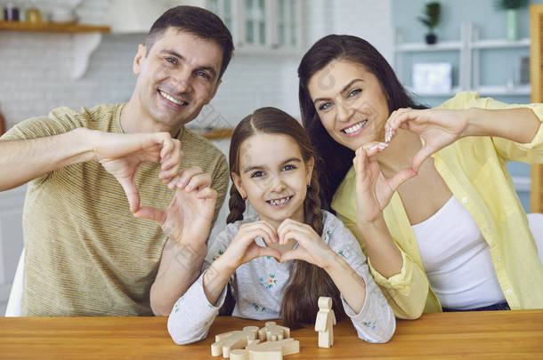 快乐的微笑的家庭手牵着手，心形如心欢迎你坐在厨房的桌子旁
