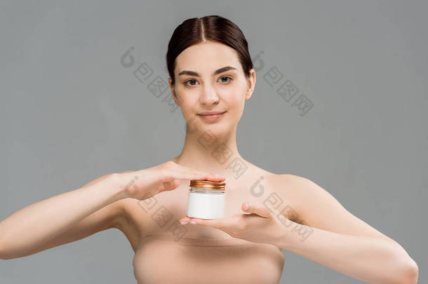 有吸引力的年轻女子拿着容器与化妆品奶油隔离在灰色 